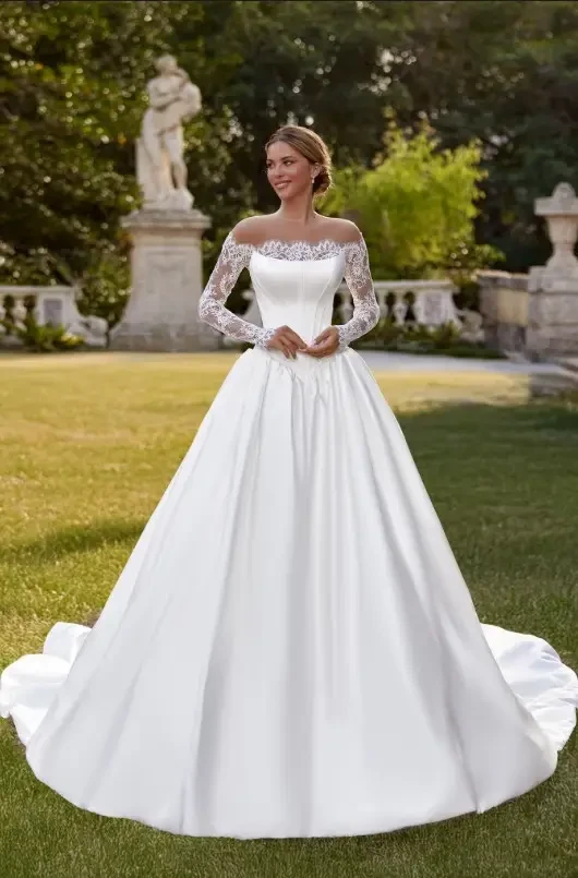 Oksana Mukha Alba Wedding Gown - Satin strapless scoop cateye Basque waist bodice with exposed boning and a pleated skirt. A lace bolero pairs with the satin gown featuring delicate eyelash lace detail.