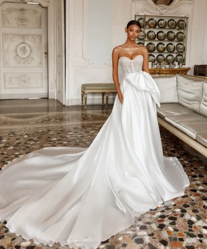 Oksana Mukha Mirella Wedding Gown - Strapless sweetheart A-Line dress with embroidered pearls and crystals on bodice with exposed boning. The skirt is lightweight organza and the dress comes with a belt that has an attached bow.