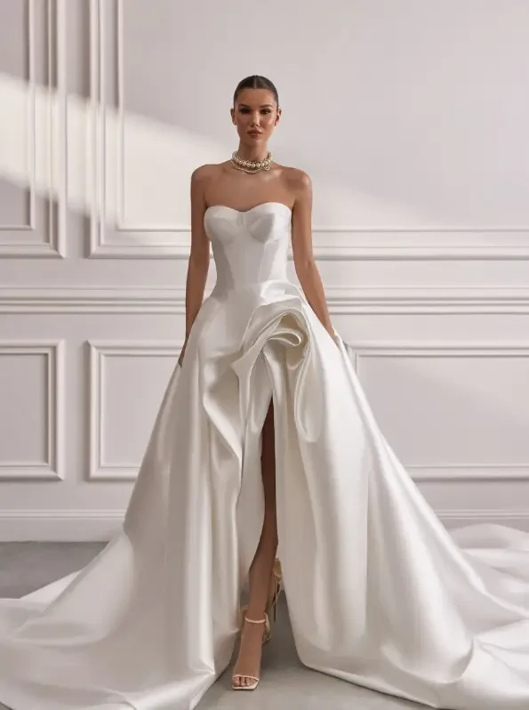 Oksana Mukha Sisley Wedding Gown featuring an A-Line silhouette made of Mikado material with a strapless sweetheart neckline and a double skirt with a short lower skirt and a long pleated skirt with drapery at the front.